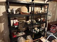 Set of two black plastic shelving units shown assembled with various items on the shelves in a basement environment.