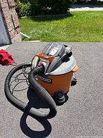 Front angle of Ridgid shop vacuum with hose coiled on the side and shadow cast on concrete.