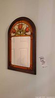 Full view of the arched stained glass mirror hanging on a wall, showing the red tulip motif and rectangular mirror below.