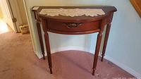 Traditional dark wood demilune console table with drawer and lace doily on top, showing front view and leg details.