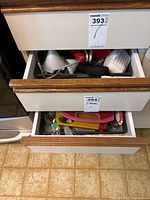Two open drawers showing various kitchen utensils including a funnel, spatulas, knives, peelers, and other tools.