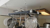 View of the black rectangular metal ceiling-mounted rack with pots, pans, and utensils hanging from S-shaped hooks on chains.