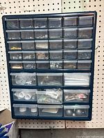 Front view showing multiple rows of small clear plastic drawers containing various metal and plastic small parts like screws, nuts, bolts, washers, and plumbing fittings.