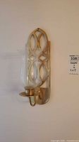 Close-up of one brass and glass wall sconce showing geometric brass backplate and clear glass hurricane shade.