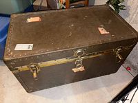 Top and front view of vintage trunk showing metal rivet detailing, locking latches, and worn label spots on surface.