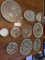 Overview of nine vintage pressed and cut glass plates and bowls arranged on wood table, showing various patterns and shapes.
