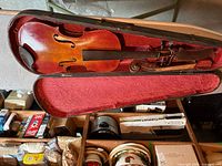 Full view of violin inside protective case with red fabric lining, items surrounding case not included