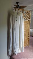 Full view of the white wool cape hanging, showing its length and shape.