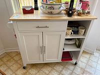 Front view of kitchen cart showing drawer, two-door cabinet, open shelves and caster wheels.