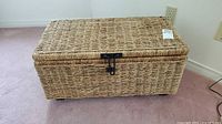 Front view of wicker storage trunk with latch closure on carpeted floor.