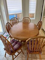 Wooden dining table with six chairs around it, all in medium oak finish. Purple plaid seat cushions on chairs.