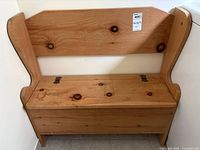 Front view of the pine wood storage bench placed against wall, showing the natural wood grain and hinges on the lift-top seat.
