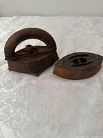 Two antique cast iron sad irons placed on a cloth surface, showing general condition and shape.
