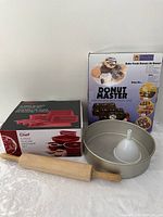 Photo showing boxed 5-piece silicone bakeware, Wilton round pan, Donut Master box, and wooden rolling pin