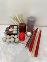 Lot of various candles on white lace surface showing wide variety including jar candle, taper candles, tealights, and pillar candles
