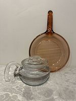 Corning Vision pan and Pyrex teapot shown side by side on table against white background.