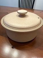 Side view of round covered casserole dish with lid showing speckled beige exterior and knob handle with steam vent.