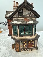Front view showing bay windows with Santa figure inside alongside detailed wooden door and snow patches on roof.