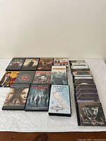 Photo showing 15 DVD and video cases arranged on a white surface, featuring titles such as 'Ten Commandments', 'Gladiator', 'Inception', 'Visiting With Bill Bowles', and 'California's Golden Coast' VHS tape case.