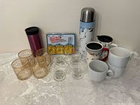 Full lot with all glassware, thermos, and mugs displayed on white patterned tablecloth