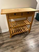 Full view of the Ikea Forhoja natural solid birch kitchen cart showing the tabletop, drawers, and slatted shelves below.