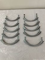 Top-down view of 10 brushed nickel curved cabinet handles arranged in two columns, each with mounting screws attached