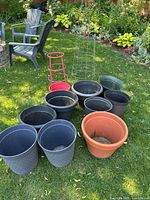 Overview of all items including nine black plastic pots, one terracotta clay pot, and three plant cages on grass.