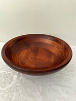Front side view of large round wooden bowl with cherry finish on a lace tablecloth.