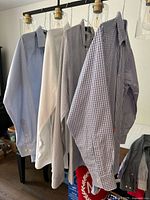 Four men's long sleeve shirts hanging on hangers: blue striped, solid white, light checked, and blue checked button-down collar shirts visible.