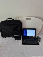 Full lot group showing Microsoft Surface tablet with attached keyboard, two black portable speakers, white lap desk, and black laptop carrying bag.