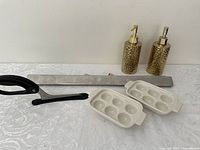 Full lot displayed together on white surface showing all items: two gold-tone soap dispensers, stainless steel wall mount holder, two white ceramic egg trays, and black-handled scissors.