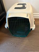 Front view of plastic pet carrier showing black metal door with latch and beige plastic body.
