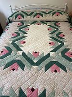 Full view of quilt laid on bed showing floral geometric pattern with pink flowers and green leaves on cream background.