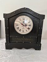 Front view showing clock face with Roman numerals and metal stud detailing on wood case.
