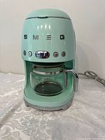 Front view of mint green SMEG coffee maker with glass carafe and chrome accents.