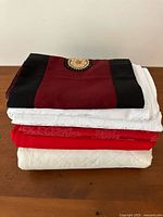 Stacked rectangular tablecloths including red with decorative pattern, solid red and white tablecloths.