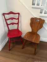Two solid wood chairs together, one red painted ladder-back and one natural wood decorative backrest chair.