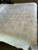 Full view of the off-white weighted blanket spread on a bed showing its size and quilted square pattern.