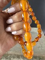 Close-up of large oval amber beads showing color and texture, held in hand to highlight size and natural inclusions.