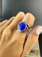 Ring worn on finger showing face and profile with blue stone and antique sterling silver design.