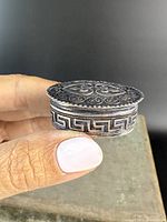 Side view of the oval sterling silver box showing detailed Greek key design on the side and overall shape.