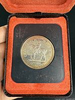 Obverse side of Canadian Silver Dollar coin featuring a horseback rider, dated 1873-1973, displayed in original red velvet-lined case.