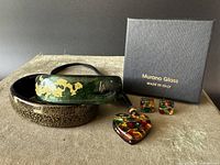 Photo of all five Murano glass jewelry pieces arranged on a fabric surface, showing two bangles, a heart pendant necklace, a pair of earrings, and the Murano Glass branded box.