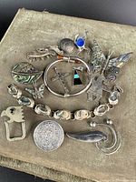Various early antique Mexican sterling silver jewelry pieces including brooches, pendants, belt buckle, and pins, laid on a beige cloth.
