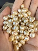 Hand holding a collection of champagne colored genuine pearls, showing irregular shapes and drilled holes