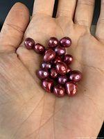 Close-up photo of a hand holding 16 genuine cherry colored pearls with a shiny surface and irregular baroque shapes.