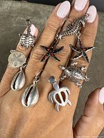 Collection of sterling silver sea life pendants displayed on hand, showing scale and detail of each pendant including starfish with opal inlay, turtles, seahorse, sand dollar, and cowrie shells.