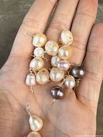Close-up photo of several individually wire-wrapped genuine pearls in various shades held in palm, showing detail of pearl sizes and silver wire loops.