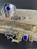 Group photo of the collection showing cuff bracelet, multiple pins, rings, and pendants on fabric background