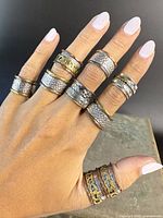 Hand displaying 7 distinct spinner rings, showcasing textures and mixed metals, including brass and copper accents.